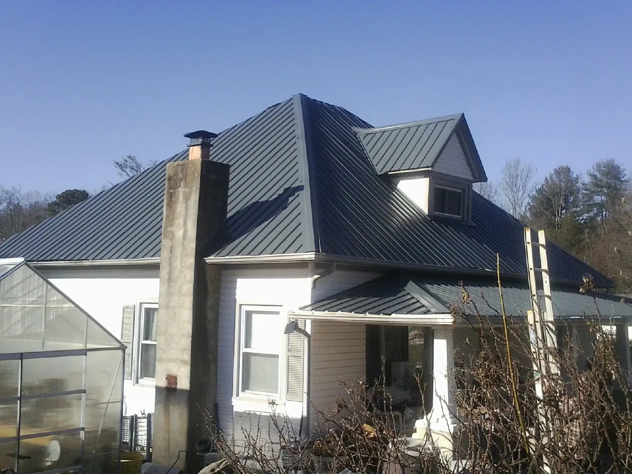 Dark blue standing seam metal roof on a white farmhouse with dormer — Slate & Tile Roof Repair by Roofing Brothers in Olive Branch