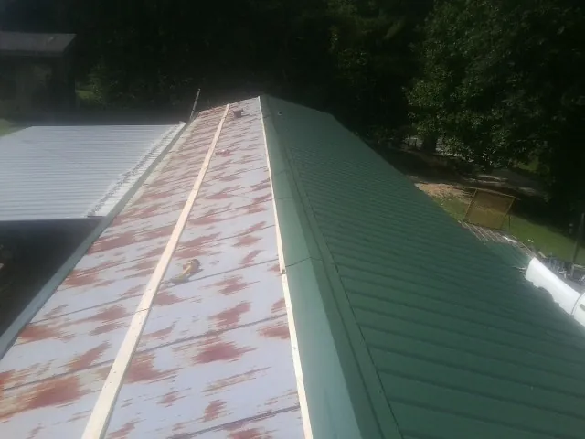 Old rusted panels beside newly installed green metal roofing — Wind Damage Roof Repair by Roofing Brothers in Olive Branch