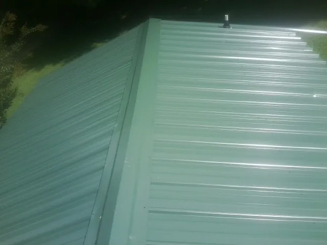 New green metal panels meeting at the ridge of a roof — Flat Roof Repair work by our crew in Olive Branch