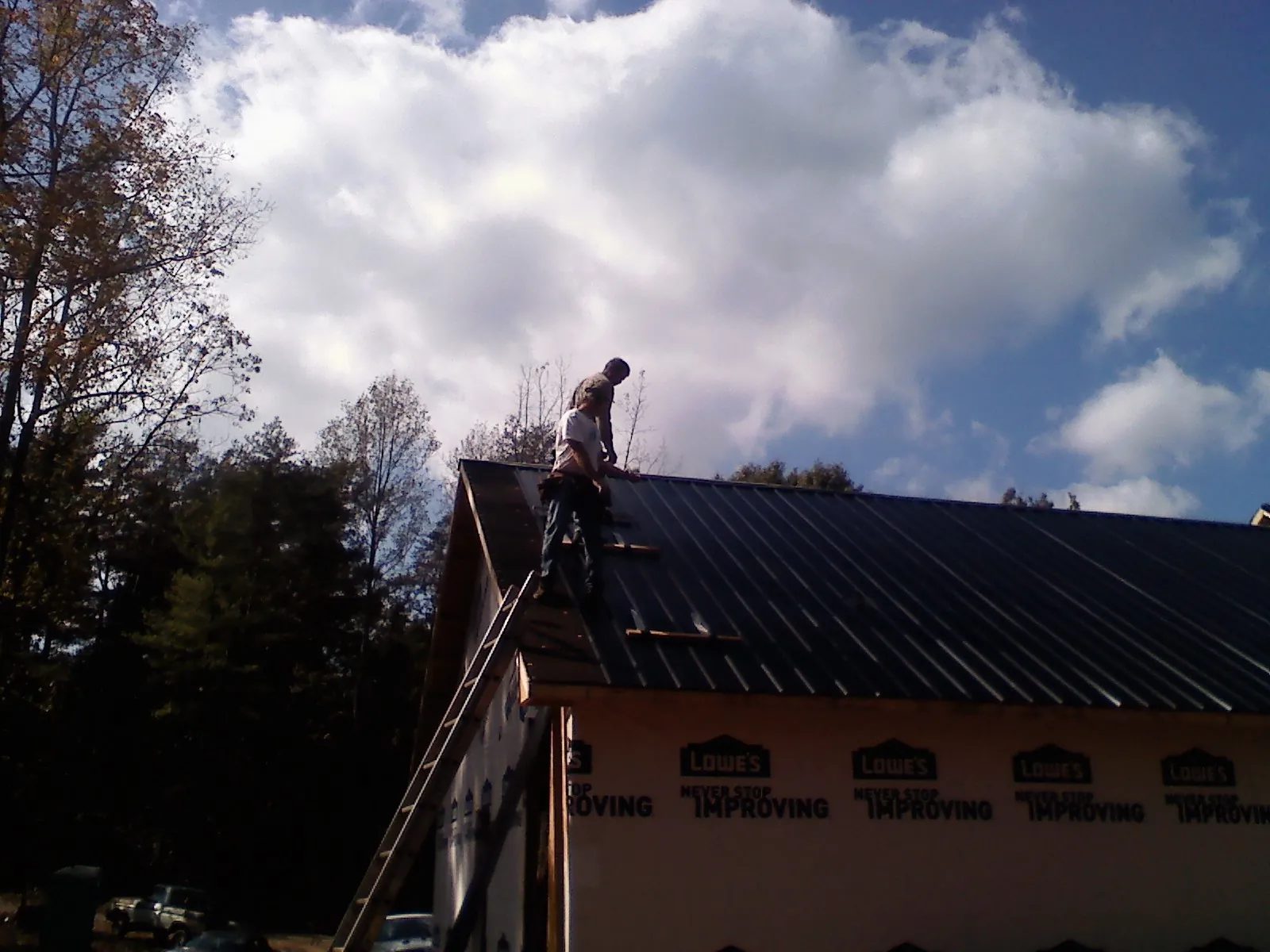 Roofer fastening dark metal panels high against a cloudy sky, from a Roof Inspection job in Olive Branch