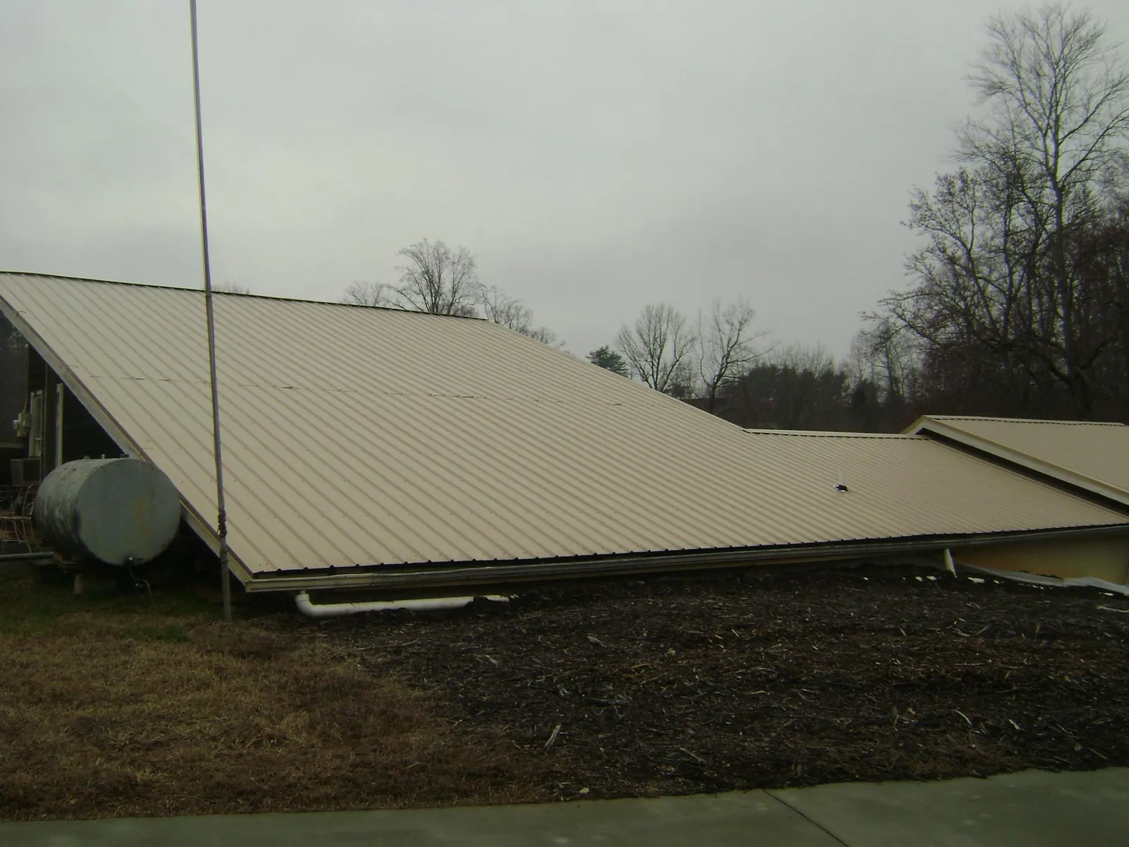 Wide tan metal roof plane seen from the ground beside a propane tank in Olive Branch