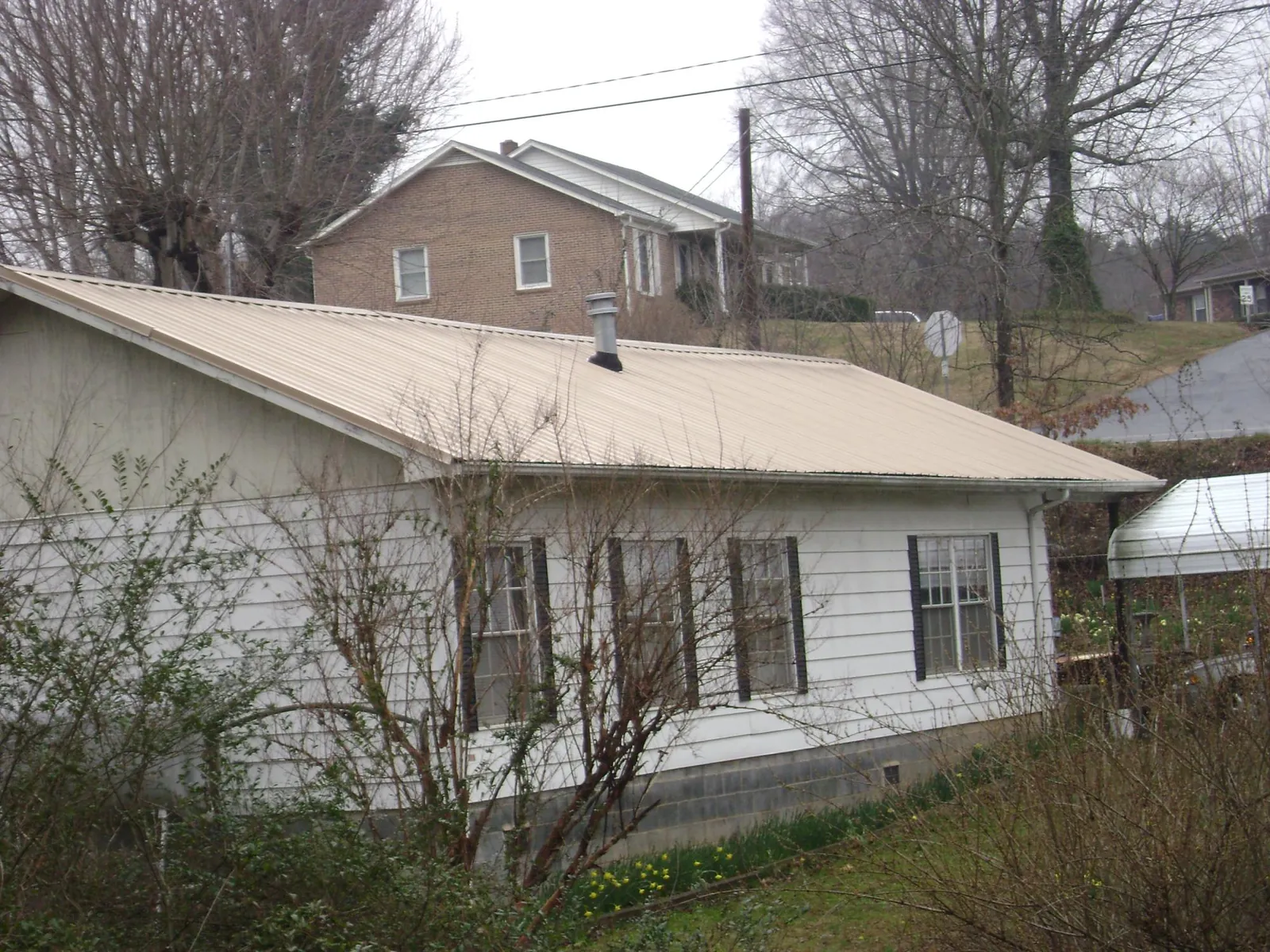 Tan metal roof on a white sided house set into a hillside — Commercial Roofing by Roofing Brothers in Olive Branch